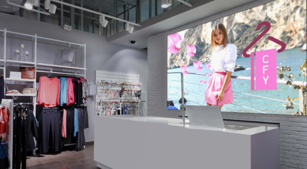 Retail clothing store interior featuring a wall-mounted LED SEG lightbox with an illuminated fabric graphic behind the checkout counter.