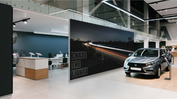 Large illuminated SEG lightbox wall display in a modern car showroom showcasing a backlit fabric graphic behind a vehicle.